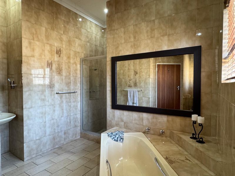 A spacious bathroom featuring a built-in bathtub, a separate shower enclosure, and a wall-mounted basin, finished with neutral-toned wall and floor tiles.