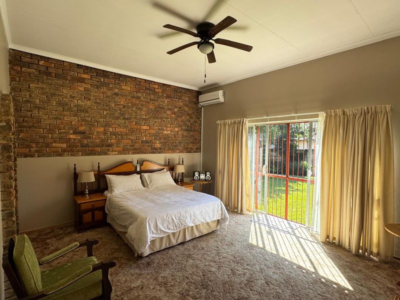 Spacious bedroom featuring an exposed brick accent wall, ceiling fan, air conditioning, and direct access to the garden through sliding glass doors.