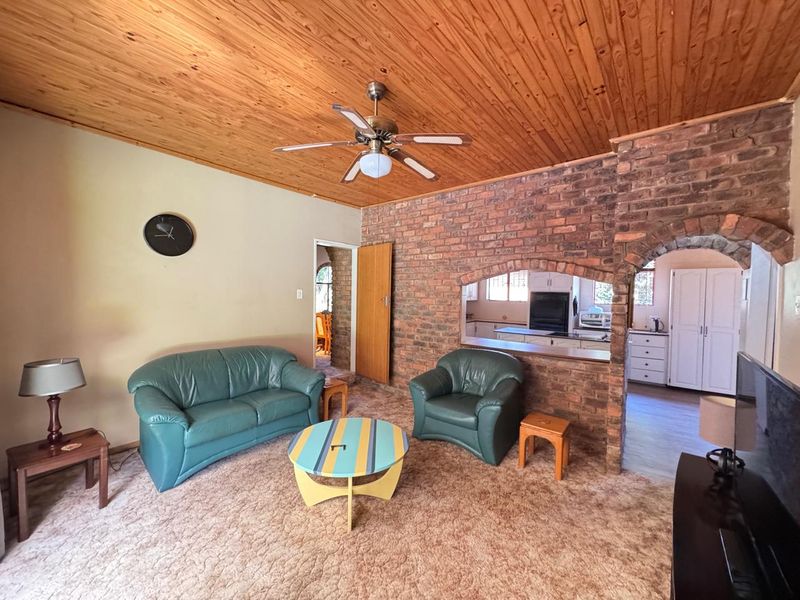 Living room featuring a timber ceiling, exposed brick wall with a pass-through window to the kitchen, and carpeted flooring.