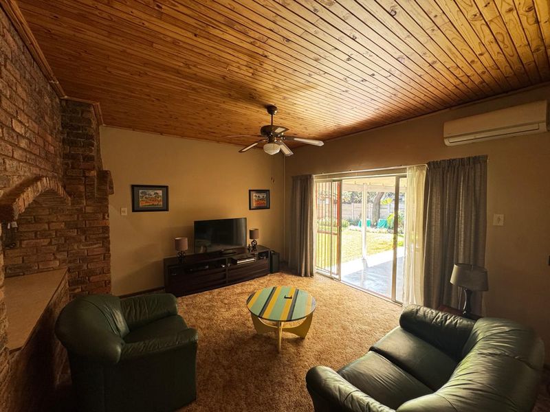 A living room featuring a timber ceiling, exposed brick fireplace, split system air conditioning, and sliding door access to the rear patio.