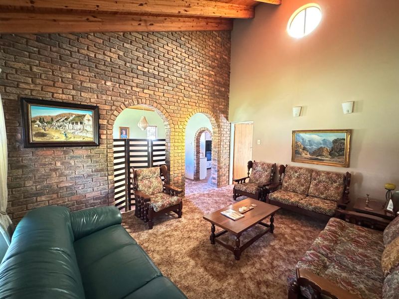 Spacious living room featuring a high exposed timber beam ceiling, a prominent brick feature wall with arched doorways, and a unique circular window.