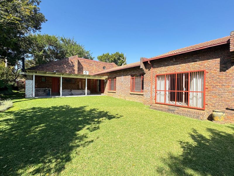 Rear view of a face brick house featuring a covered patio area, well-maintained lawn, and secure window bars.
