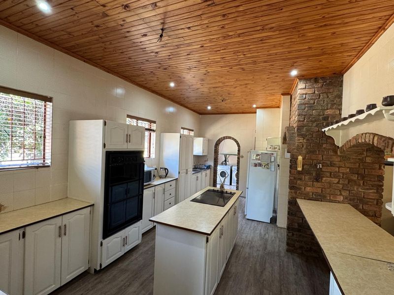 Spacious kitchen featuring a central island, built-in oven, exposed brick chimney feature, and timber ceiling, offering a rustic aesthetic with functional layout.