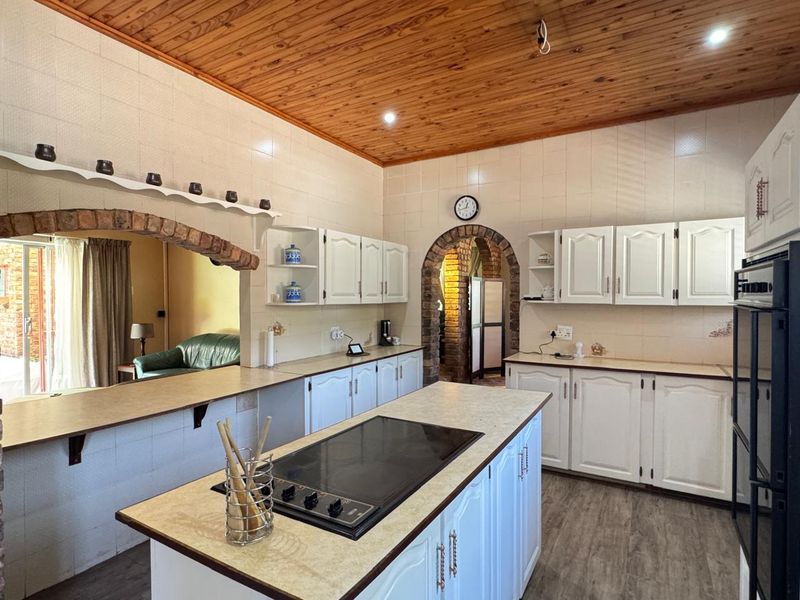 Spacious kitchen featuring a timber ceiling, brick archway details, a central island with a built-in hob, and ample white cabinetry.