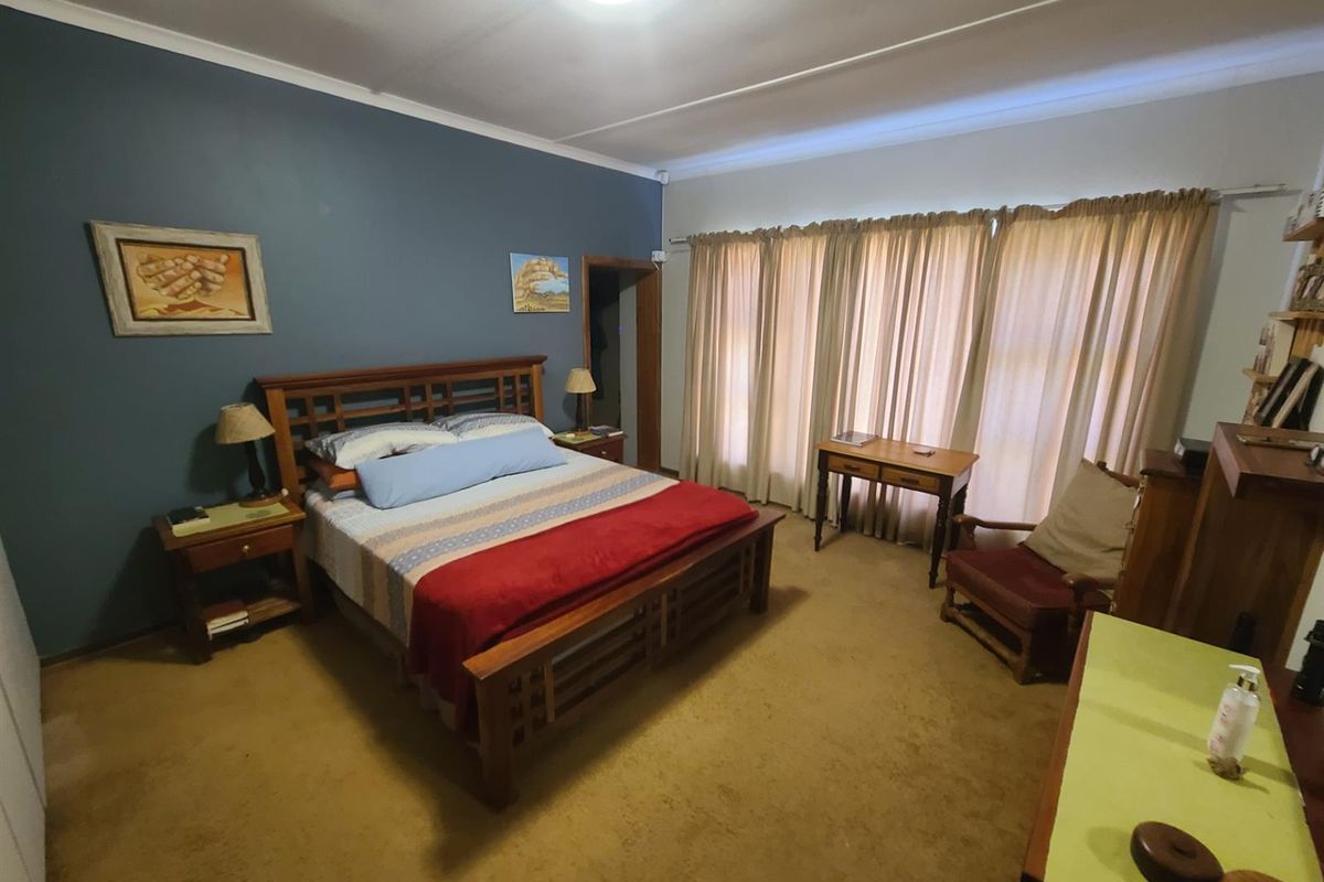 A spacious bedroom featuring carpeted flooring, a blue accent wall, and large windows with curtain tracks.