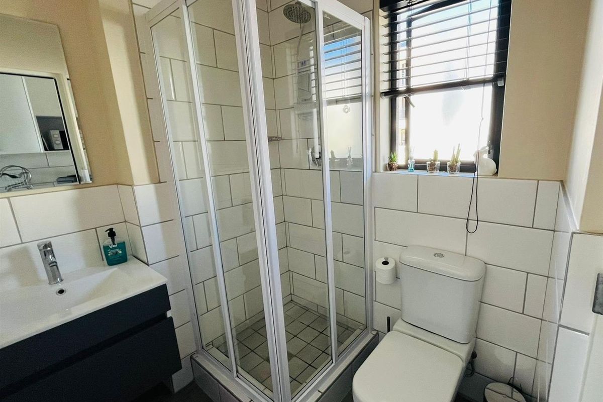 A modern bathroom featuring a glass-enclosed shower, a vanity basin with storage, and a toilet, finished with white subway wall tiles.