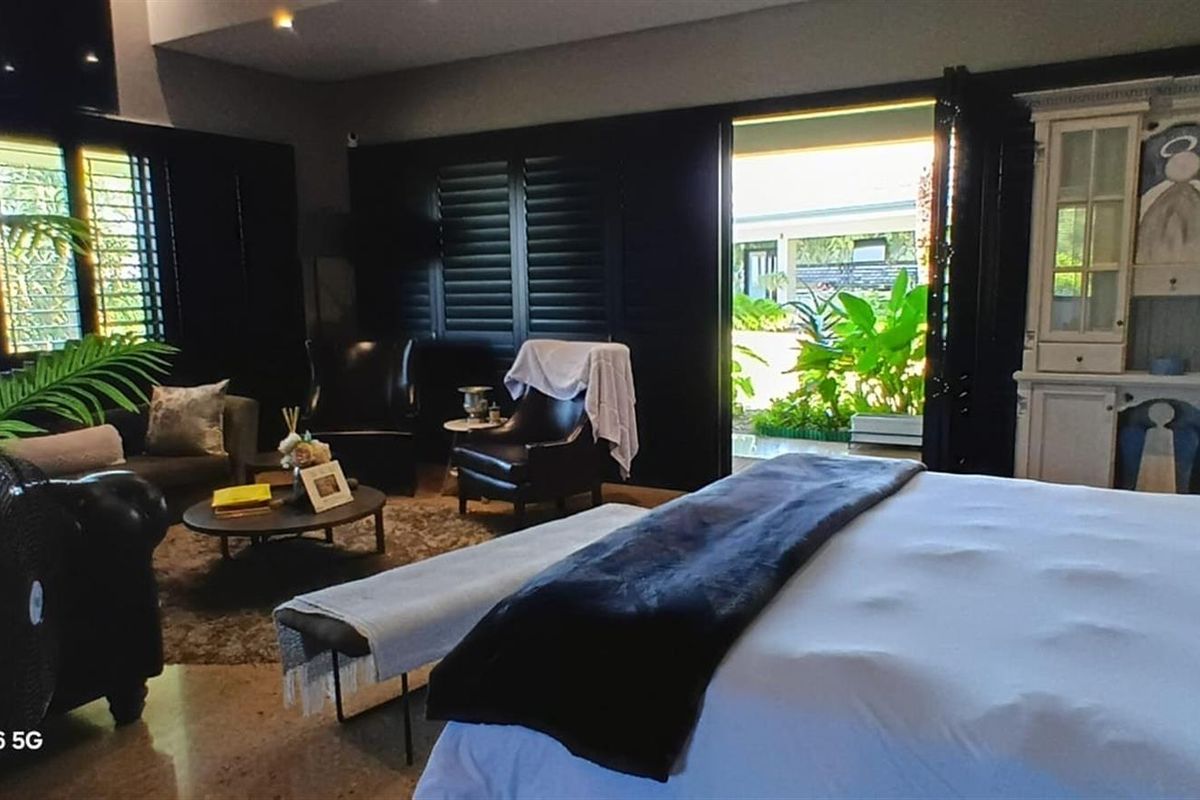 Spacious bedroom featuring dark plantation shutters and bi-fold doors opening to an outdoor area, providing a seamless transition between indoor and outdoor living spaces.