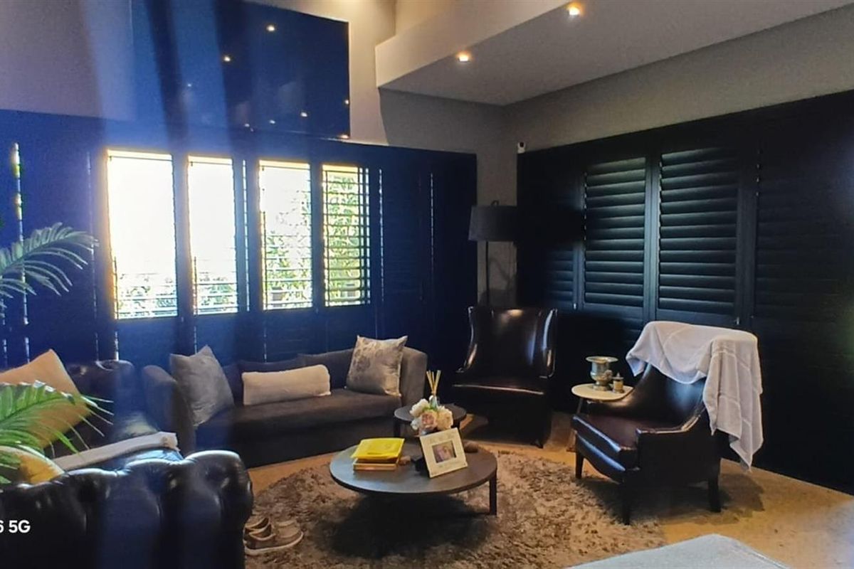 A well-maintained living room featuring dark plantation shutters, recessed lighting, and large sliding glass doors providing access to the outdoor area.