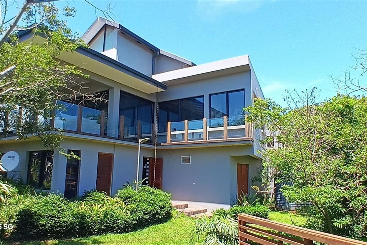 A modern two-story residential property featuring a rear balcony with glass balustrades, large aluminium windows, and a well-maintained garden area.