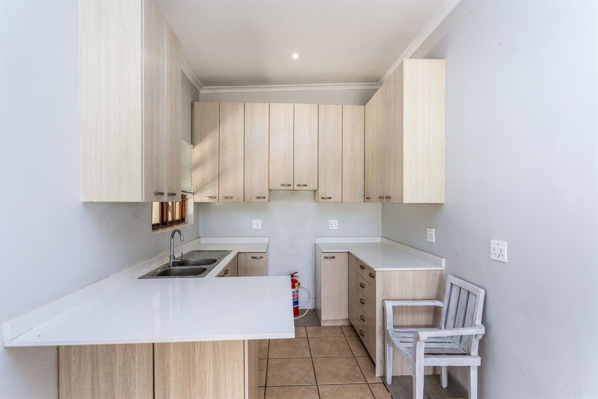 A functional kitchen featuring light wood-finish cabinetry, white countertops, a double-basin sink, and tiled flooring.