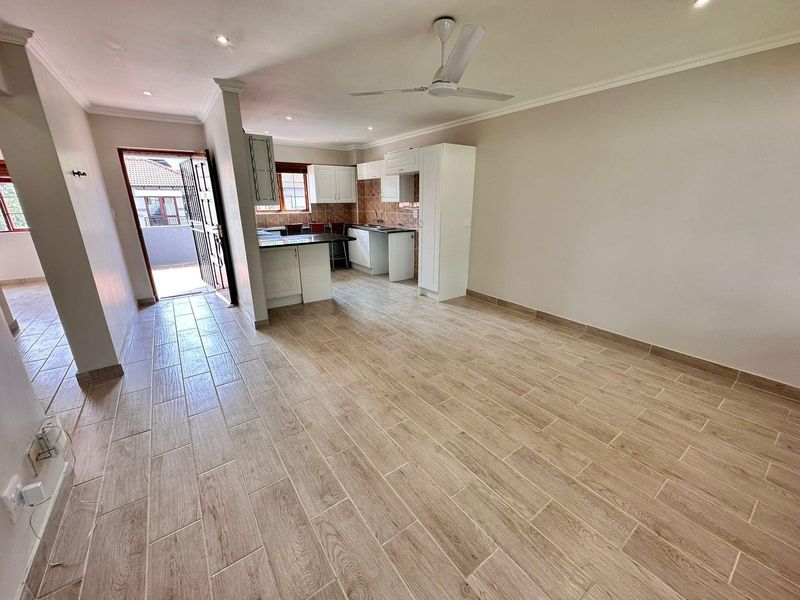 Spacious open-plan living area featuring modern wood-look tiled flooring, recessed lighting, a ceiling fan, and a functional kitchen with granite countertops.