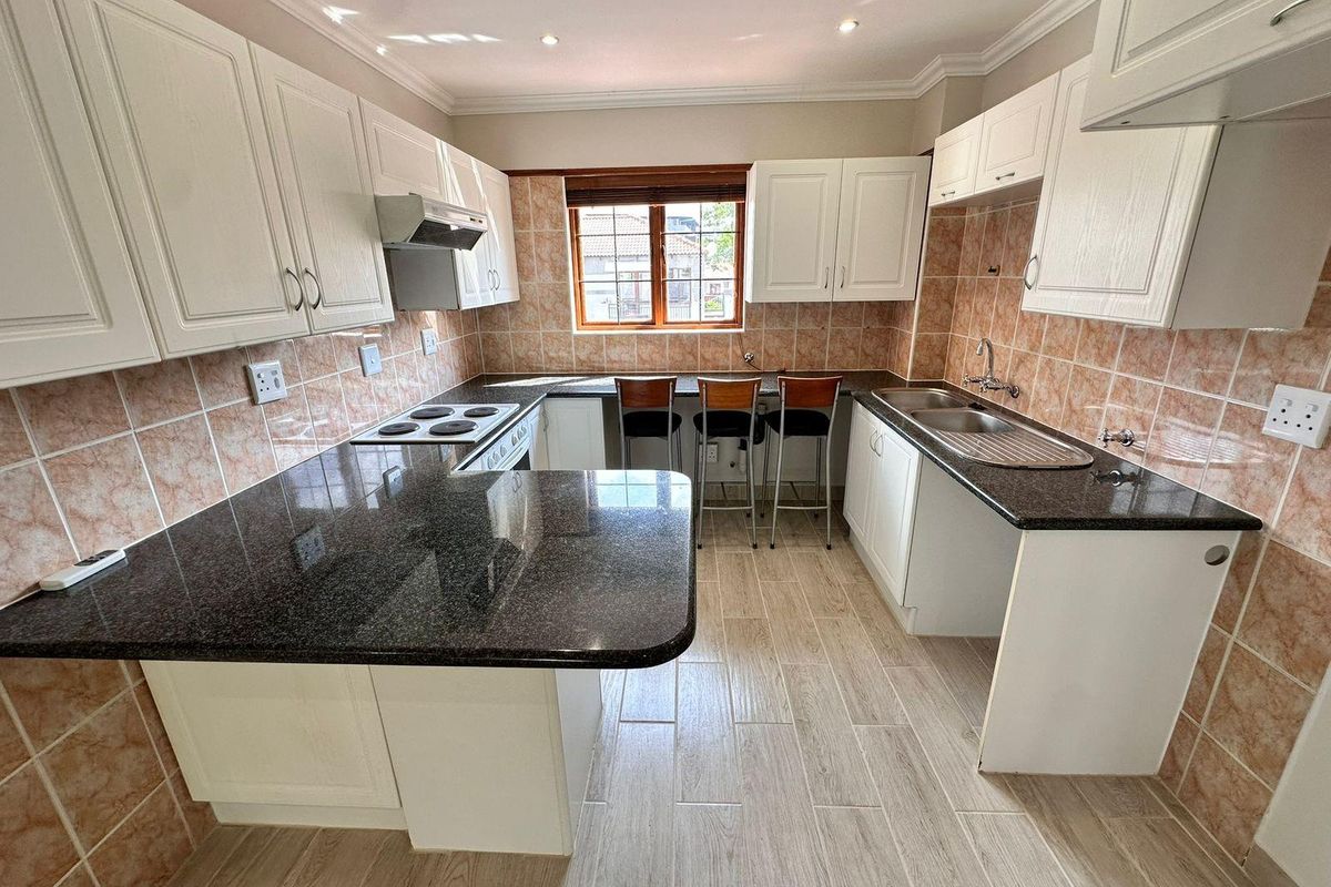 A functional kitchen featuring white cabinetry, dark granite countertops, a breakfast bar, and tiled backsplash with integrated hob and extractor fan.