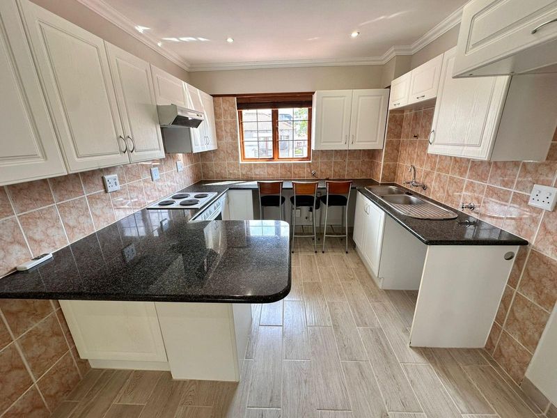 A functional kitchen featuring white cabinetry, dark granite countertops, a breakfast bar, and tiled backsplash with integrated hob and extractor fan.