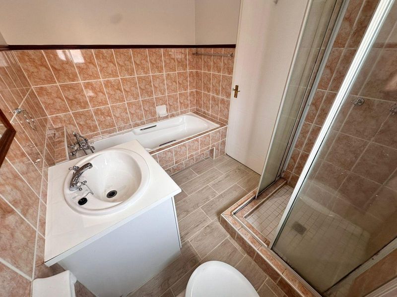 A functional bathroom featuring a built-in bathtub, separate shower enclosure, and a vanity basin with tiled finishes throughout.