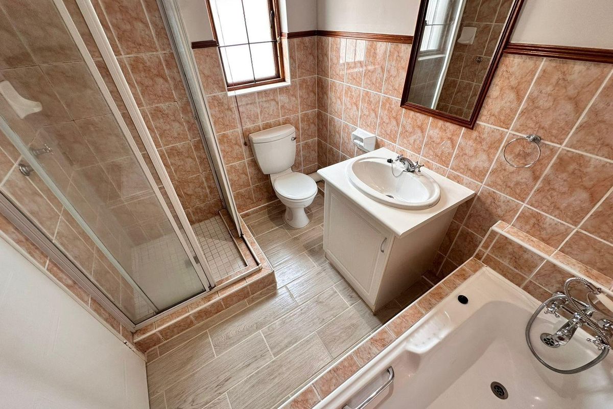 A functional bathroom featuring a separate shower enclosure, bathtub, vanity cabinet with washbasin, and tiled finishes throughout.
