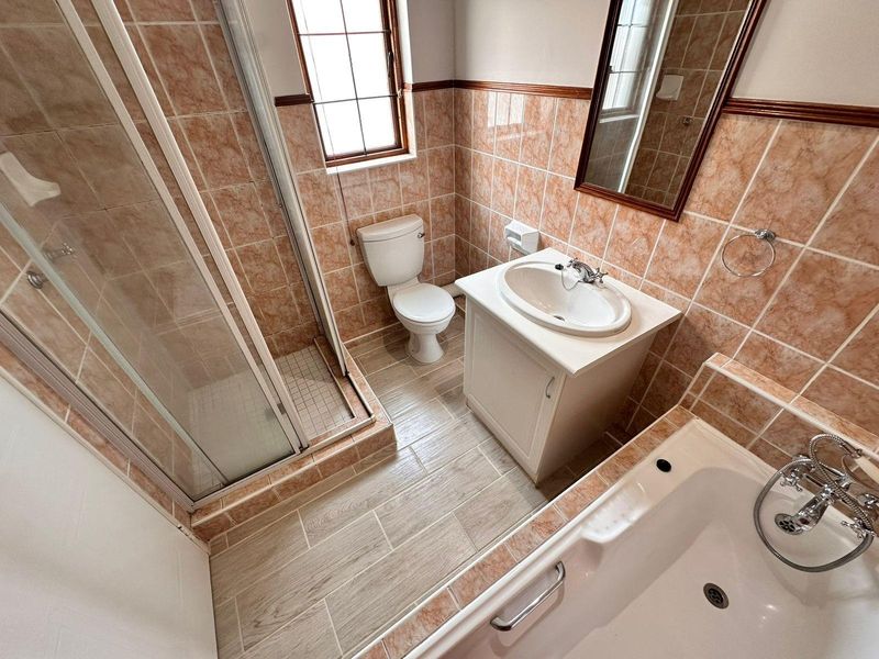 A functional bathroom featuring a separate shower enclosure, bathtub, vanity cabinet with washbasin, and tiled finishes throughout.