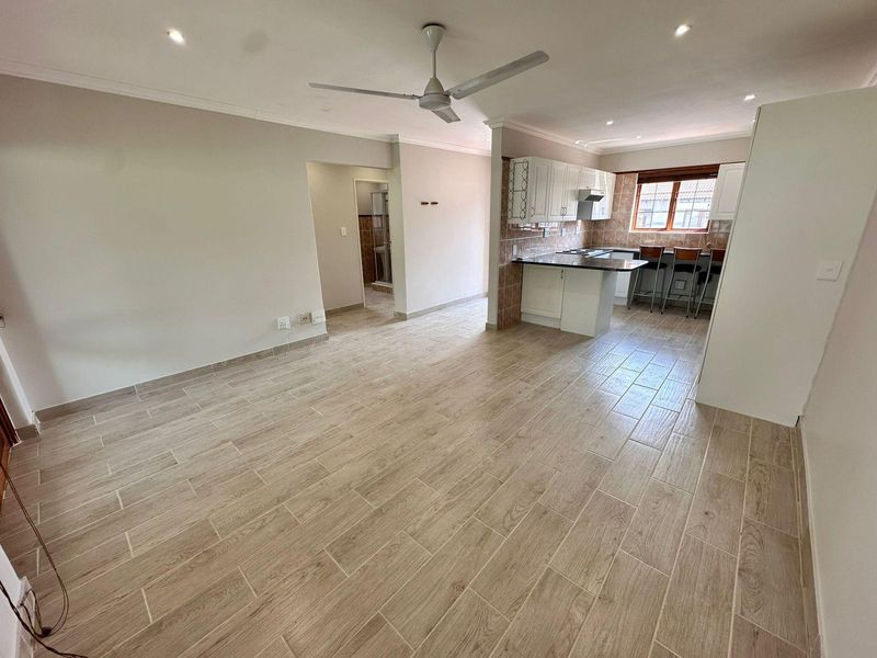 Spacious open-plan living area featuring modern wood-look tiled flooring, a ceiling fan, and a functional kitchen with breakfast bar and built-in cabinetry.