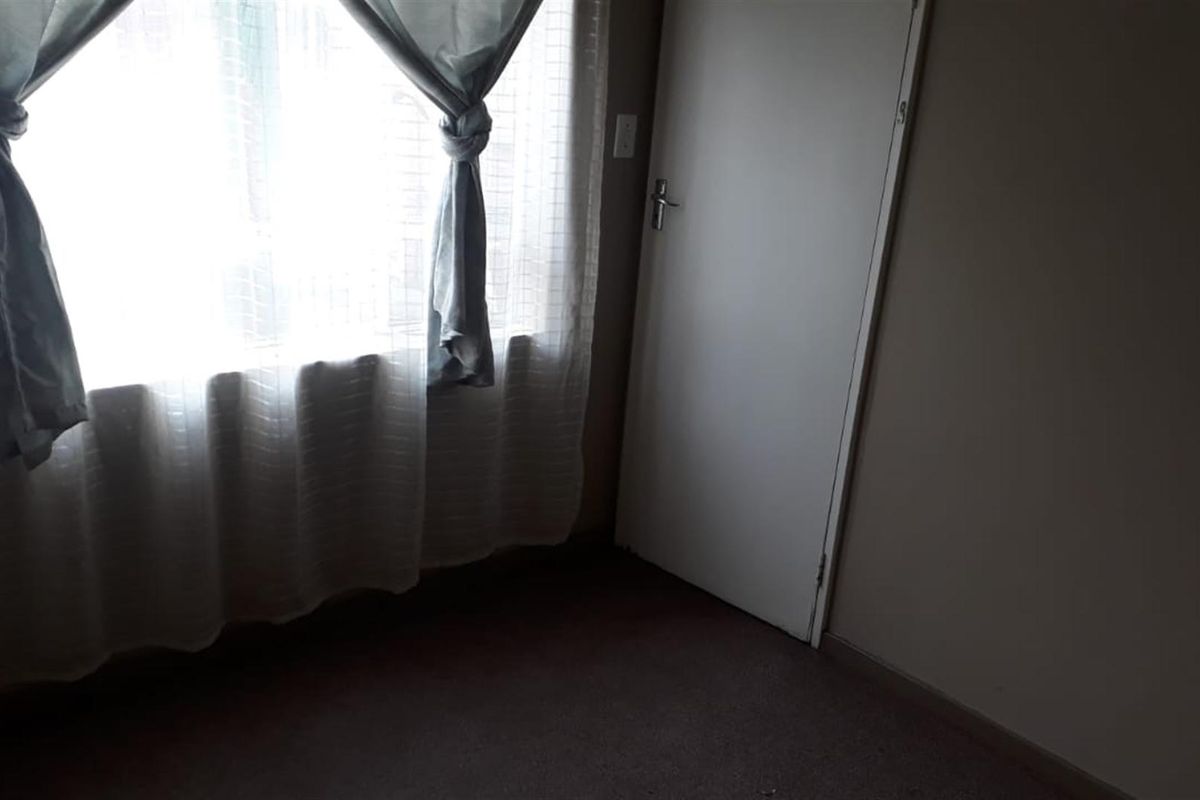 A simple bedroom interior featuring carpeted flooring, a window with curtains, and a standard internal door.