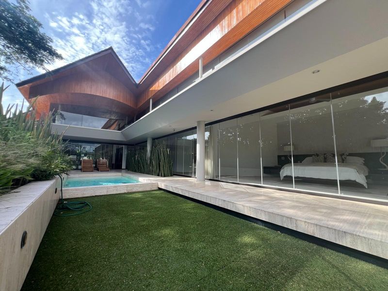 A modern rear exterior view featuring a sleek swimming pool, stone patio, and expansive glass sliding doors opening into the residence.