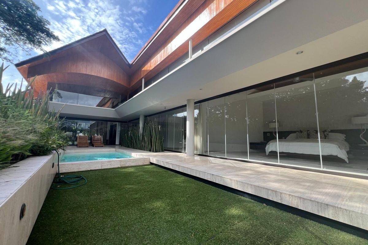 A modern rear exterior view featuring a sleek swimming pool, stone patio, and expansive glass sliding doors opening into the residence.