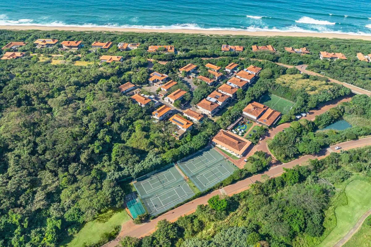 Aerial view of a coastal residential estate featuring tennis courts, landscaped grounds, and proximity to the beach.