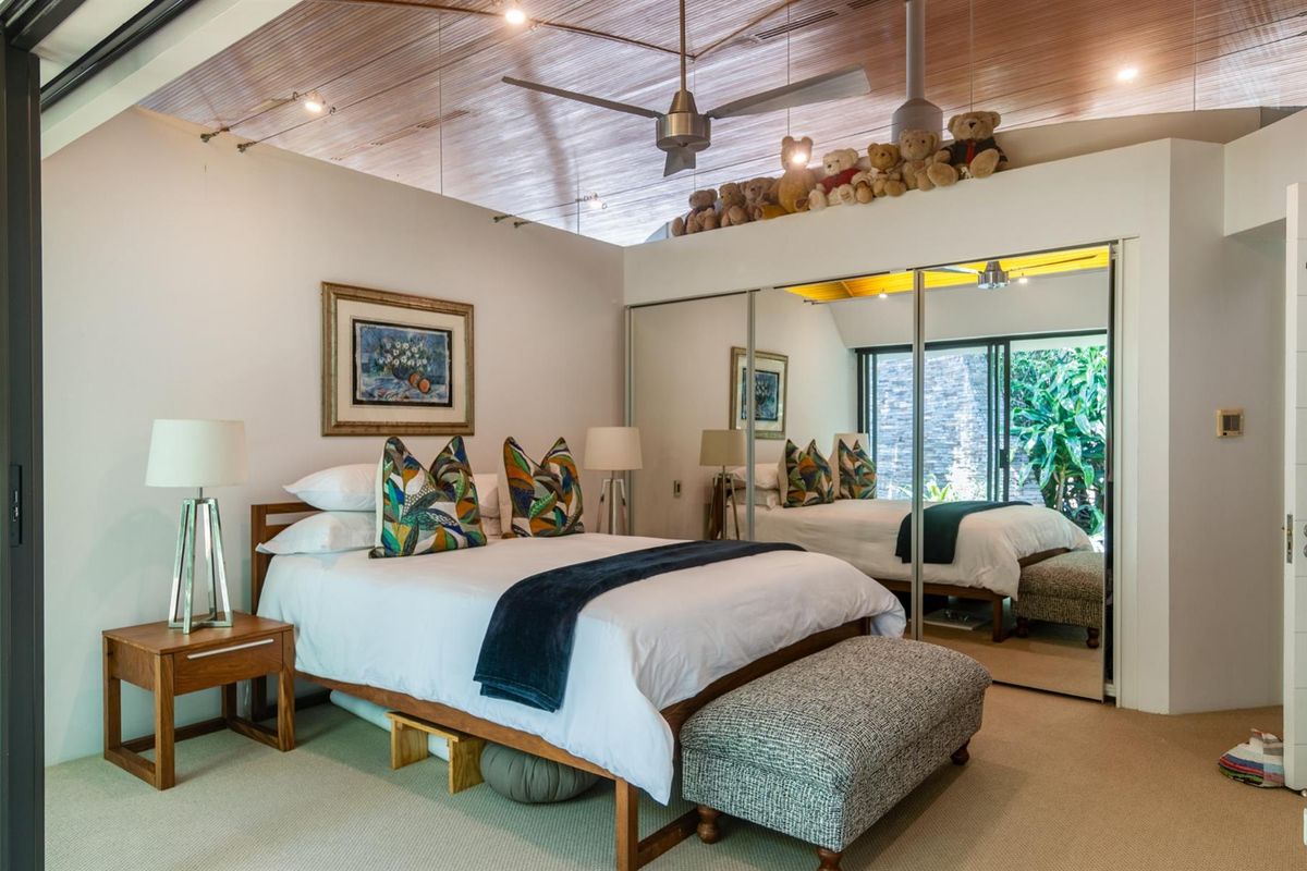 A well-lit bedroom featuring a unique timber-paneled vaulted ceiling, ceiling fan, and large mirrored built-in wardrobes with direct access to an outdoor area.