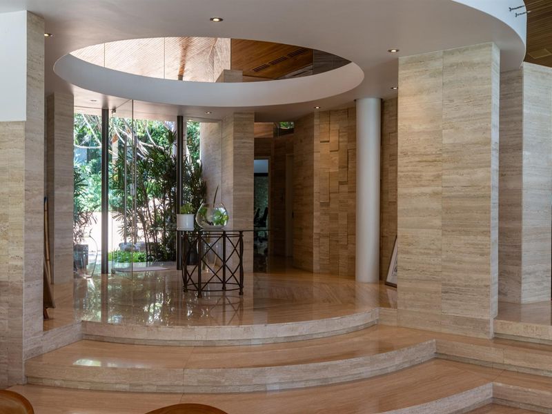 Elegant entrance hall featuring travertine stone flooring, a circular recessed ceiling detail with integrated lighting, and a glass door leading to the garden.