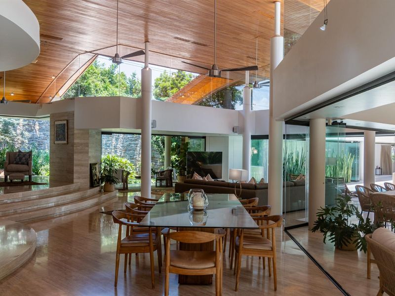 Spacious open-plan living and dining area featuring high timber-clad ceilings, polished stone flooring, and expansive glass walls opening to the garden.