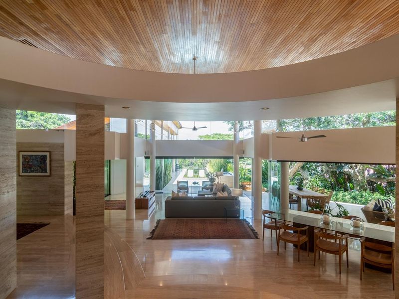 Spacious open-plan living and dining area featuring high-end travertine flooring, a striking circular timber-clad ceiling, and seamless indoor-outdoor flow to the garden.