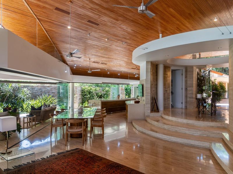 Spacious open-plan living area featuring a vaulted timber-clad ceiling, polished stone flooring, and seamless indoor-outdoor flow through large glass sliding doors.