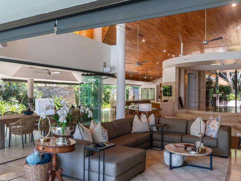 Expansive open-plan living area featuring high timber-lined ceilings, stone flooring, and seamless indoor-outdoor flow to a covered patio through large sliding glass doors.
