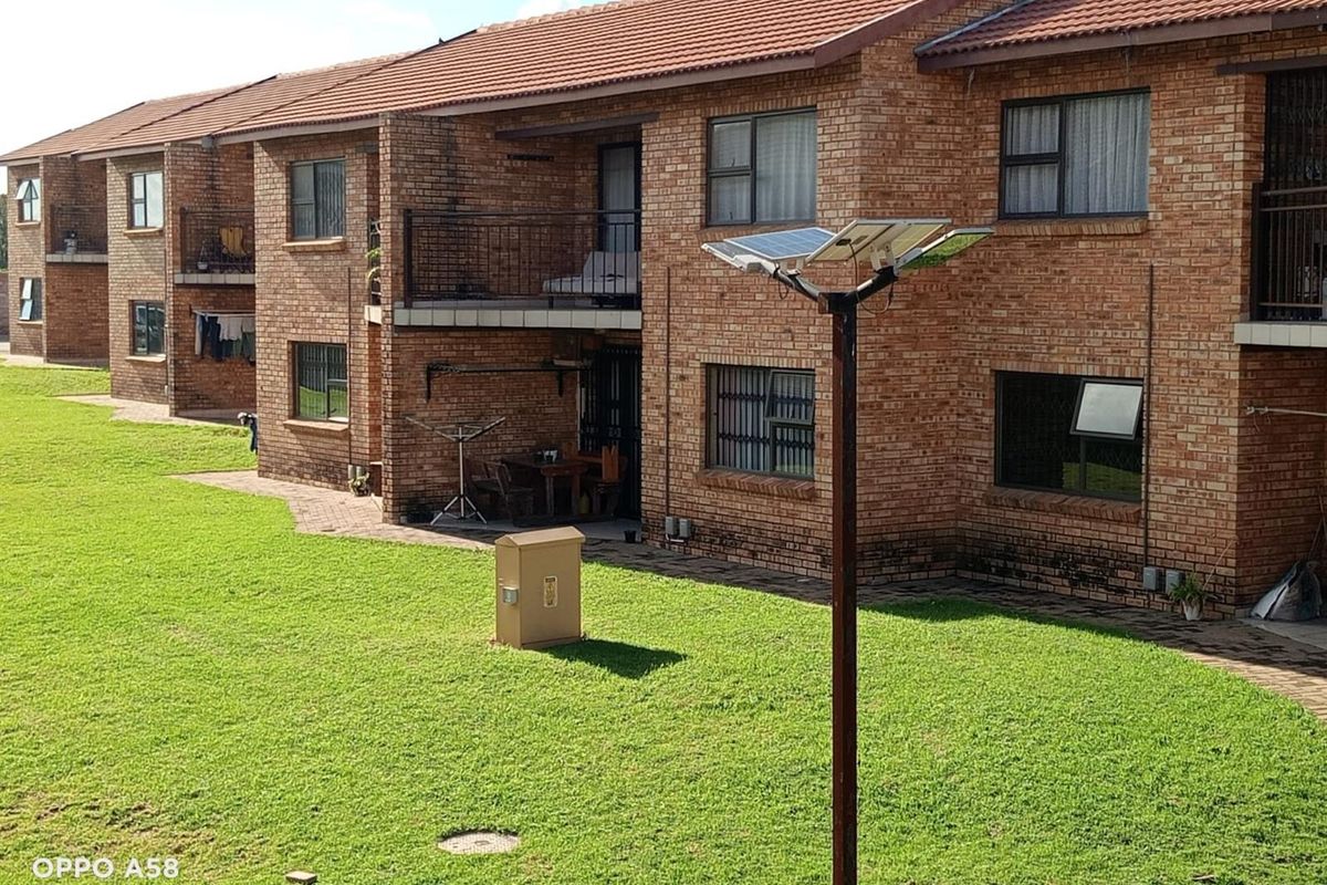 Exterior view of a multi-story brick apartment complex featuring tiled roofing, private balconies, and a shared lawn area.