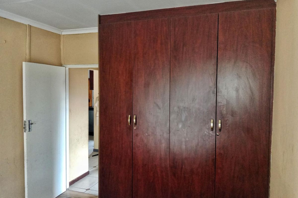 A bedroom featuring built-in wooden cupboards and neutral wall finishes, providing a functional space ready for updates.