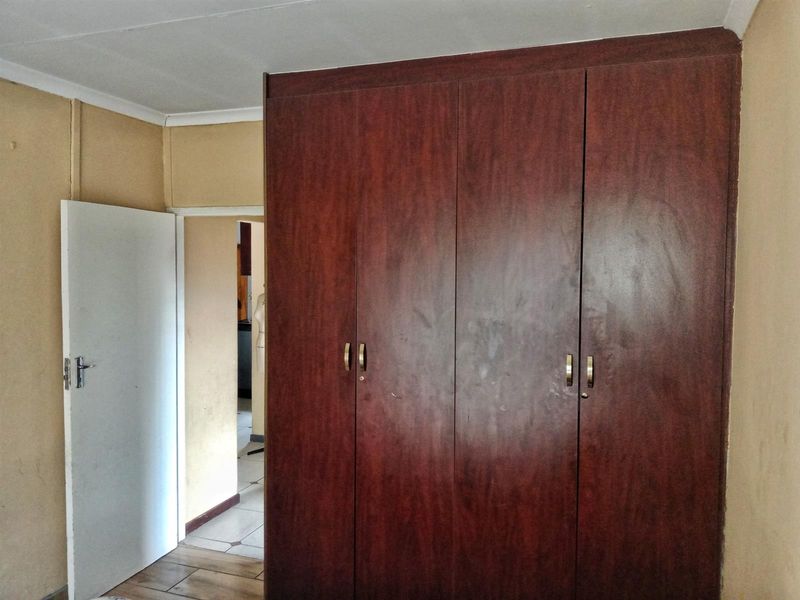 A bedroom featuring built-in wooden cupboards and neutral wall finishes, providing a functional space ready for updates.