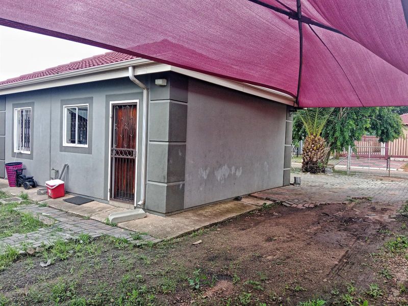 Rear exterior view of the house featuring a paved area, security gate, and a large shade sail structure.