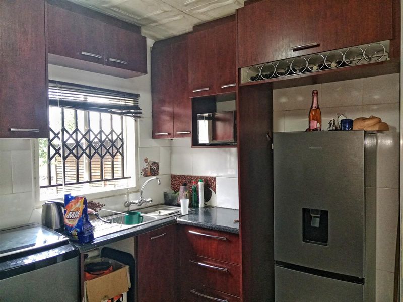 A functional kitchen featuring dark wood-toned cabinetry, laminate countertops, a stainless steel sink, and a tiled backsplash with a window security gate.