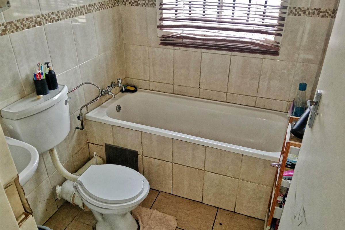 A compact bathroom featuring a standard bathtub, toilet, and pedestal basin with tiled walls and flooring, requiring some maintenance and cosmetic updates.