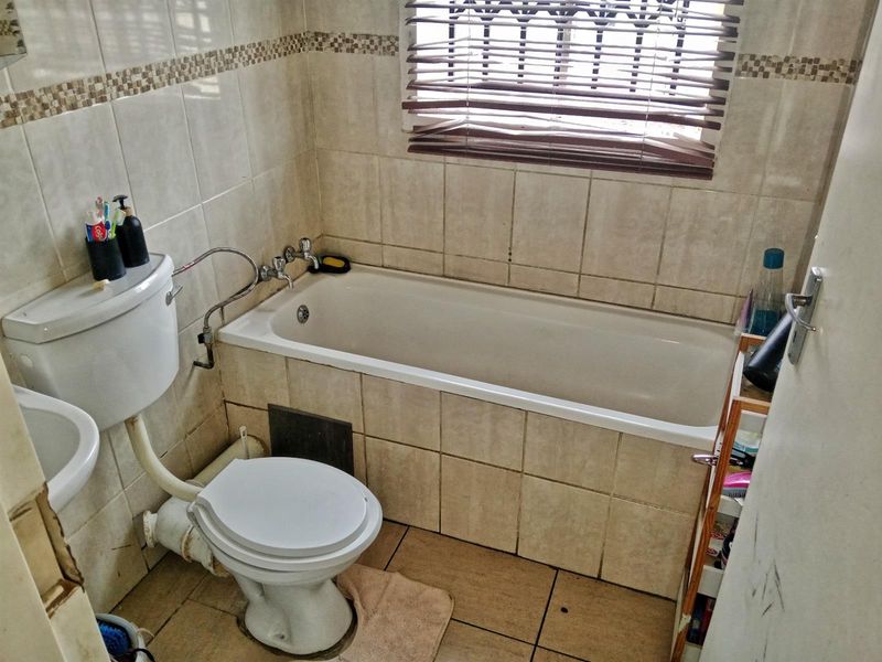 A compact bathroom featuring a standard bathtub, toilet, and pedestal basin with tiled walls and flooring, requiring some maintenance and cosmetic updates.