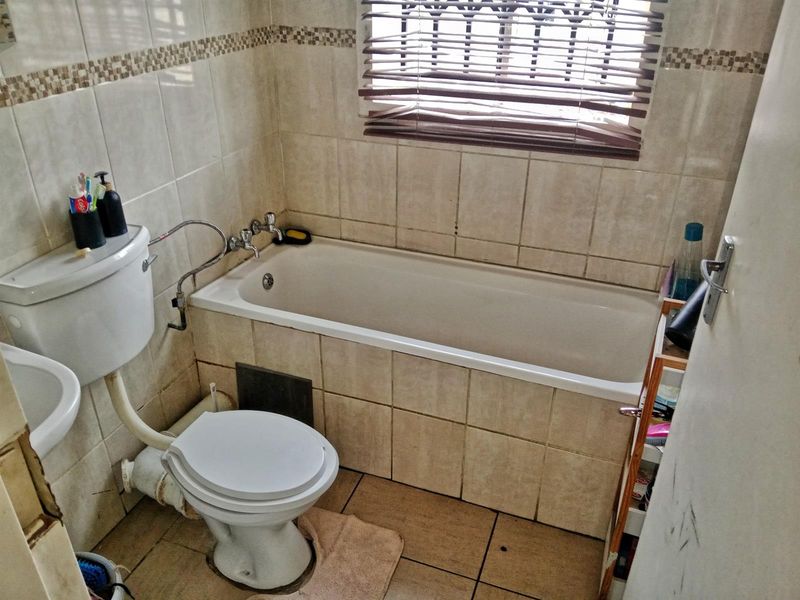 A compact bathroom featuring a bathtub, toilet, and washbasin with tiled finishes, requiring some maintenance and cosmetic updates to improve its overall condition.