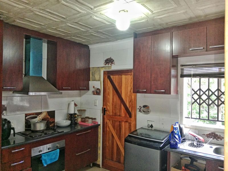 Functional kitchen featuring dark wood cabinetry, built-in oven and hob, stainless steel sink, and a tiled backsplash with a secure window.
