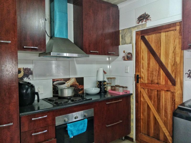 A functional kitchen featuring dark wood cabinetry, built-in oven and hob, stainless steel extractor fan, and a rustic wooden door.