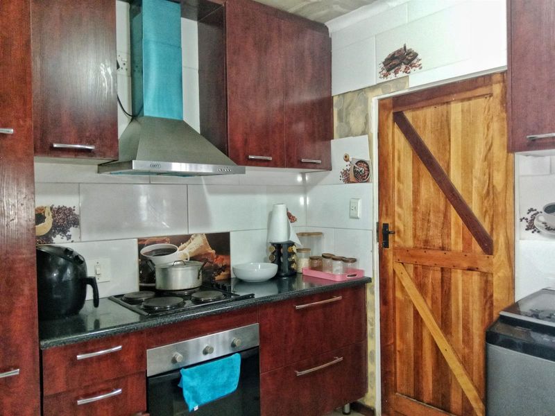 A functional kitchen featuring dark wood cabinetry, granite countertops, a built-in oven, and an electric hob with an extractor fan.
