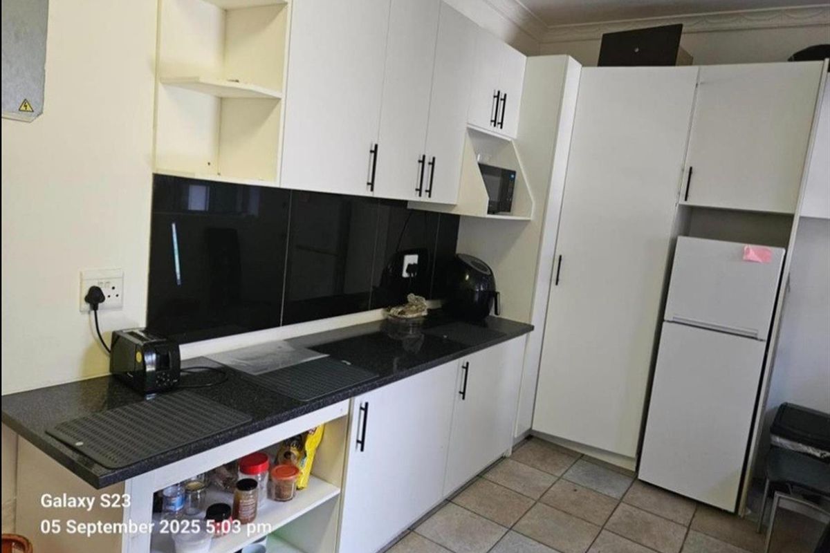 A functional kitchen featuring white cabinetry, black countertops, and a dark glass splashback with tiled flooring.