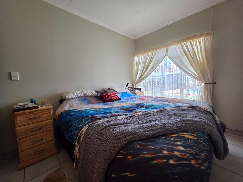A bedroom featuring tiled flooring and a large window with curtaining, providing natural light and a view of the outdoor area.