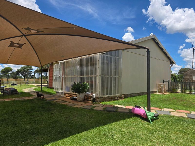 A rear exterior view of the property featuring a large shade sail over a paved area and a semi-enclosed sunroom structure.