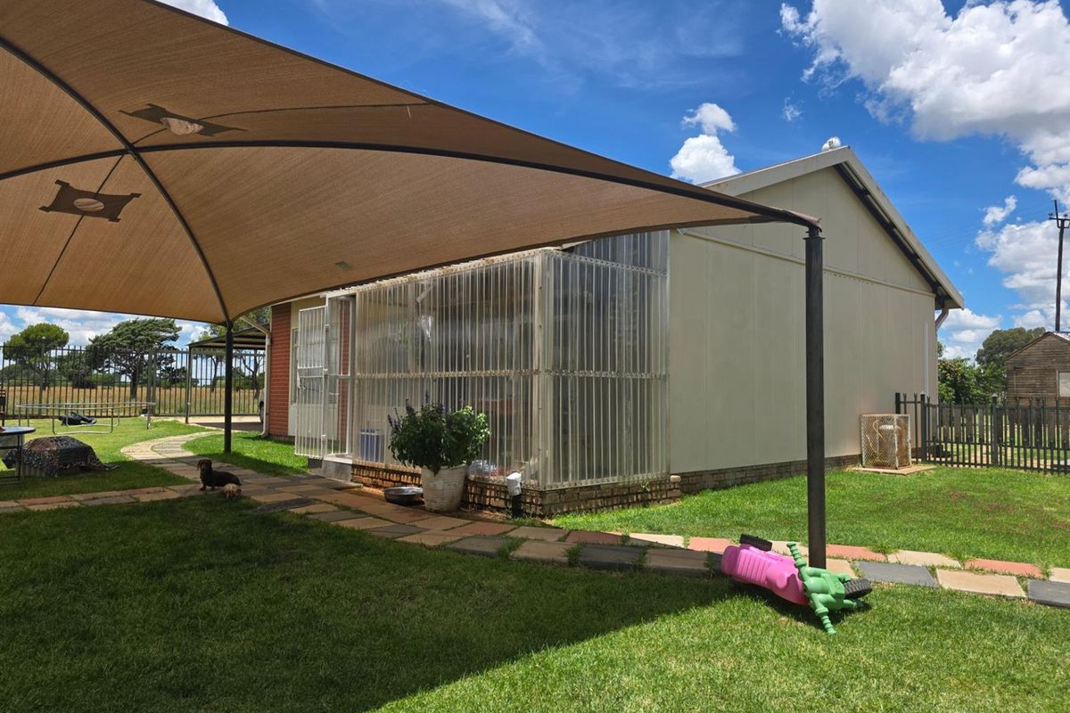 A rear exterior view of the property featuring a large shade sail over a paved area and a semi-enclosed sunroom structure.