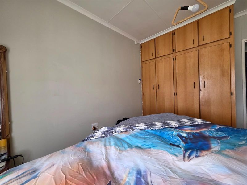 A bedroom featuring built-in wooden cupboards providing ample storage space, finished with neutral wall tones and standard ceiling cornicing.