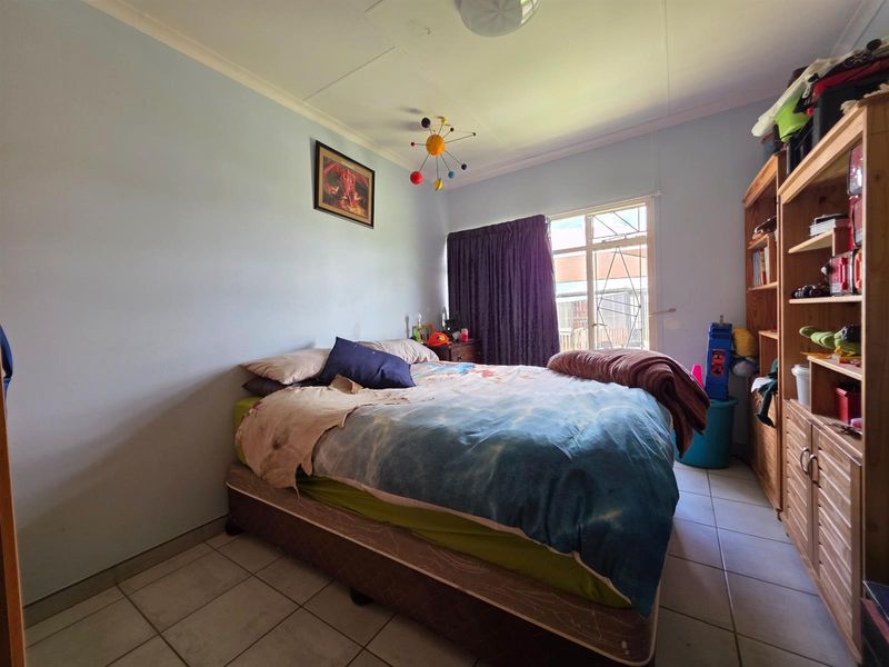 A standard bedroom featuring tiled flooring, a window with security bars, and coved ceiling detailing.
