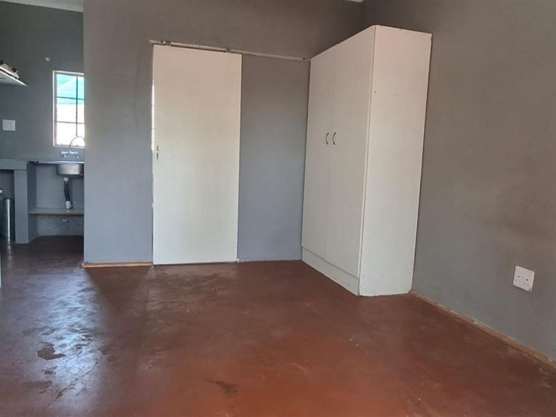 An open-plan living area featuring a basic kitchenette with a sink, built-in cabinetry, and concrete flooring.