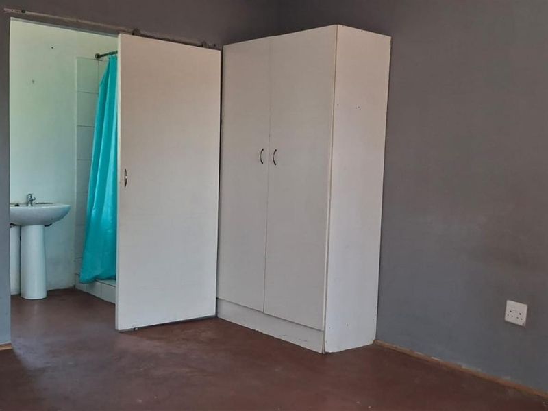 A bedroom featuring a built-in wardrobe and an en-suite bathroom with a pedestal basin and shower area.